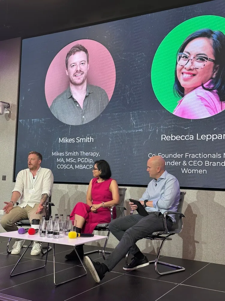 Rebecca seated on a panel beside a screen showing the speakers