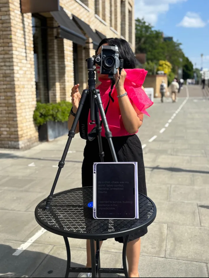 Rebecca in a pink top behind a camera on a tripod in the street