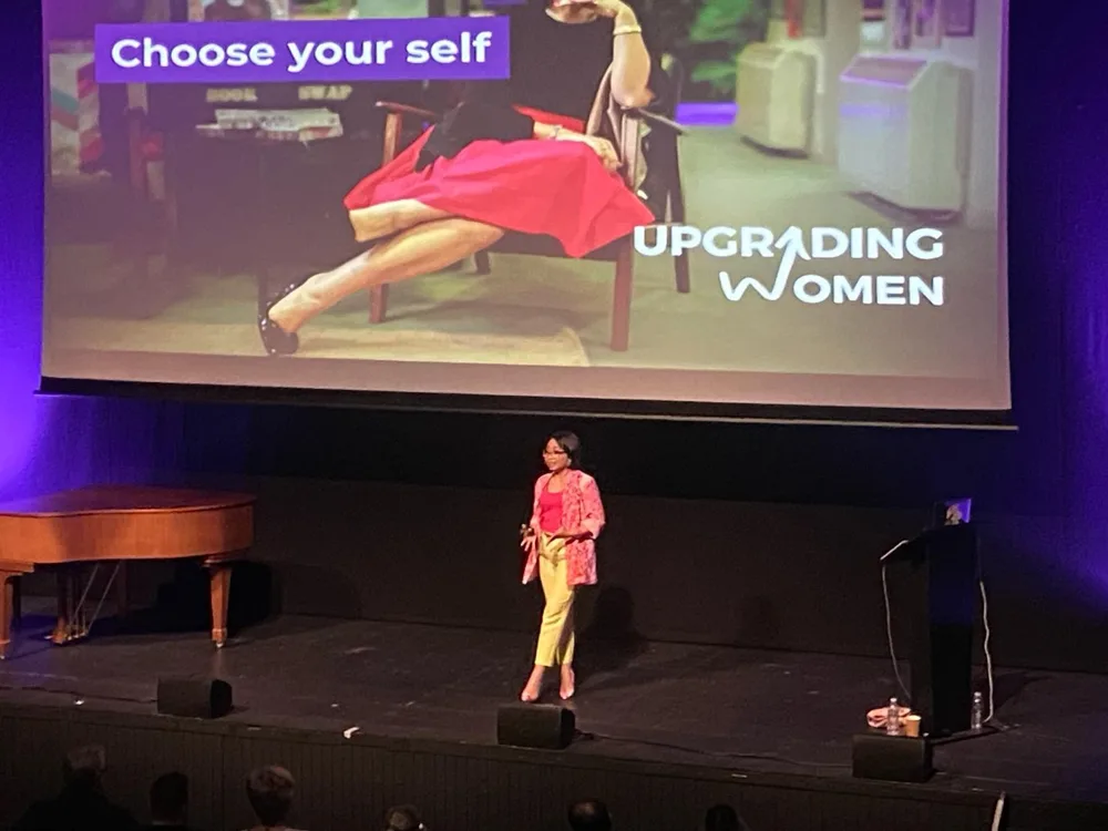 Rebecca on stage beneath an Upgrading Women Choose your self slide