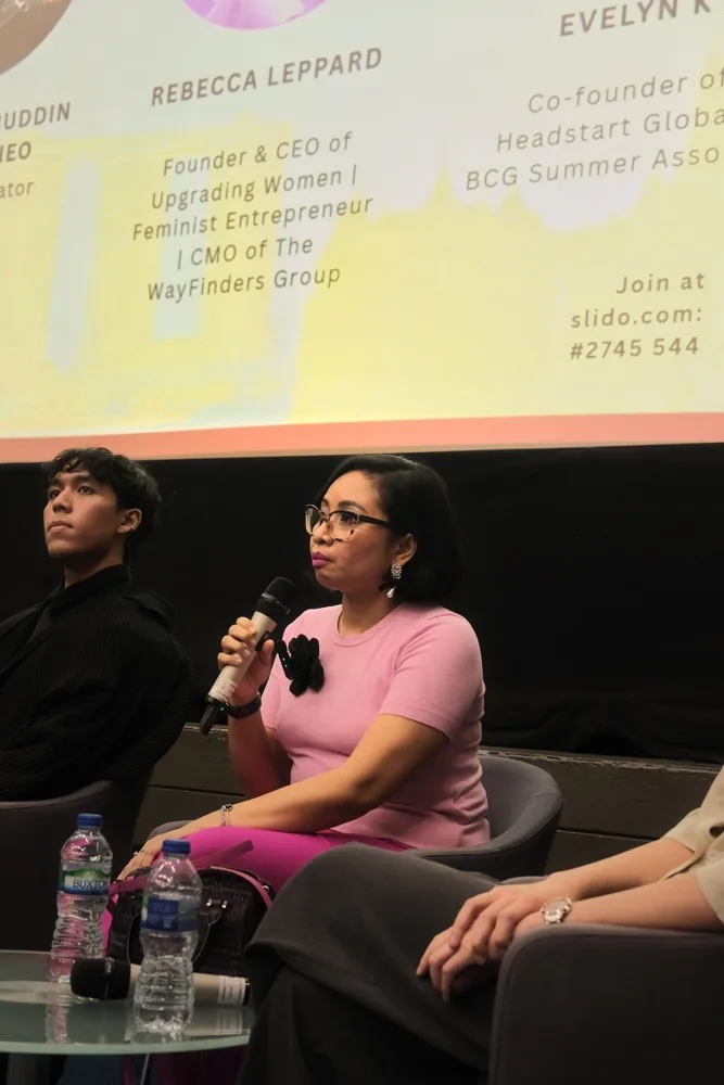 Rebecca speaking on a panel beneath a speaker banner