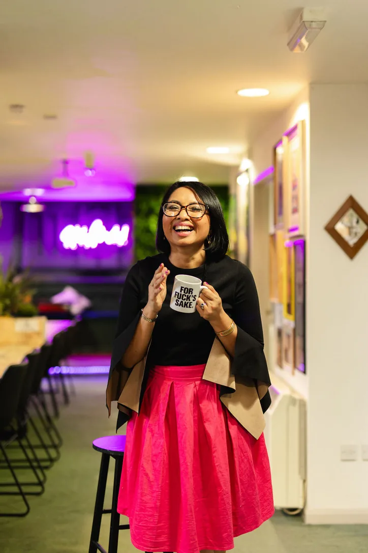 Rebecca laughing and holding a mug in a red skirt at an event