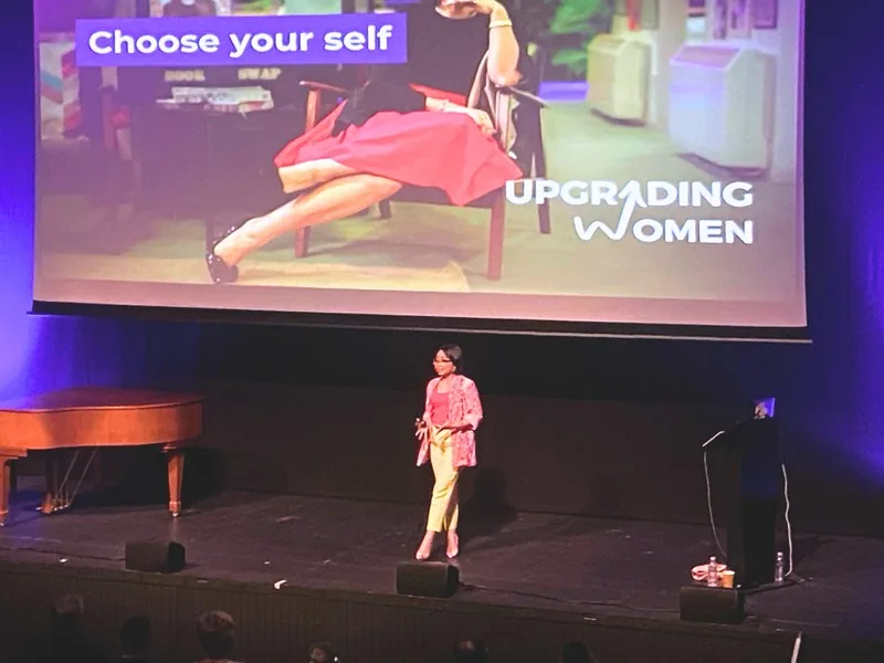 Rebecca speaking on stage in front of an Upgrading Women screen