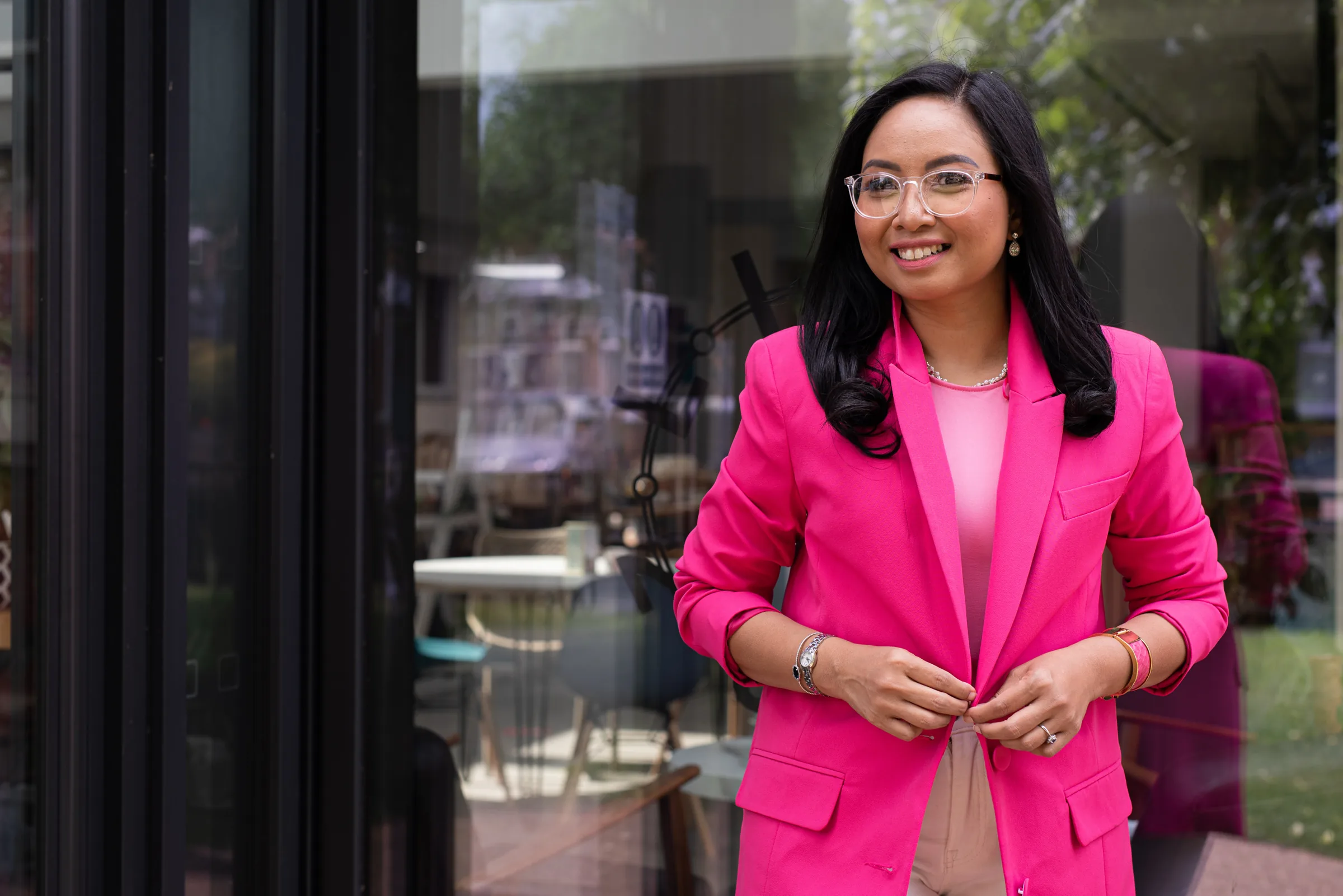 Rebecca Leppard in a pink blazer, smiling outside a glass fronted building