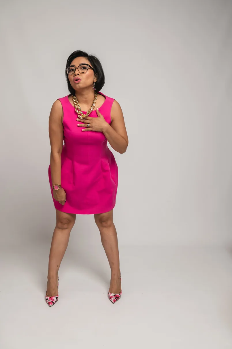 Studio portrait of a woman in a fitted pink dress against a pale grey backdrop