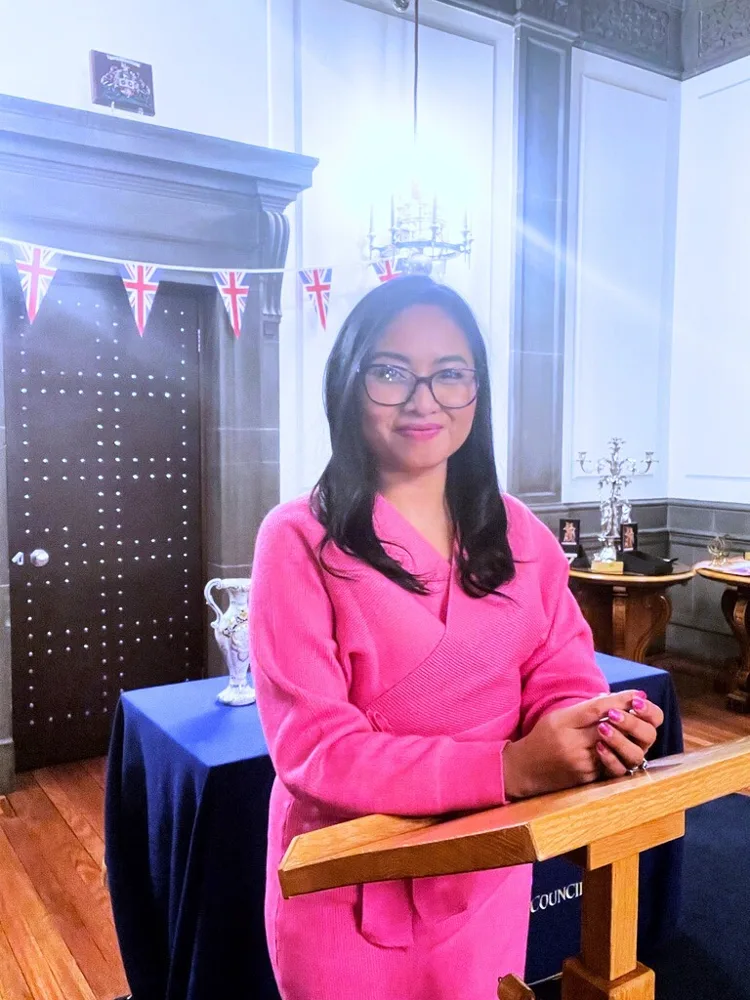 Rebecca in pink standing at a lectern in a panelled room